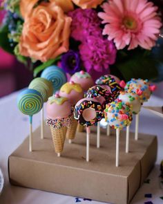 cake pops with sprinkles and candies on sticks in front of flowers