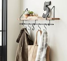 a coat rack with three coats hanging on it and two bags next to it, in front of a window