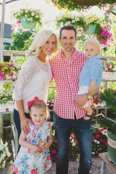 a man, woman and two children standing in front of potted plants with flowers