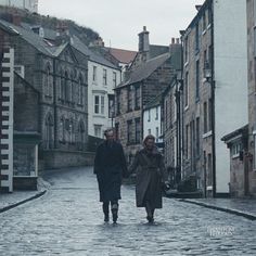 two people walking down a cobblestone street in an old european town on a rainy day