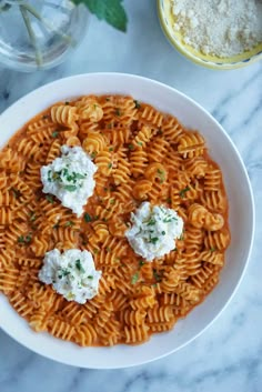 a white bowl filled with pasta and cheese on top of a marble table next to two glasses