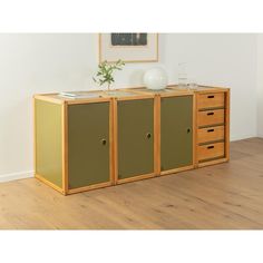 a wooden cabinet with three drawers and two vases on the top one is green