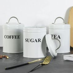 three white coffee canisters sitting on top of a counter next to a knife and fork