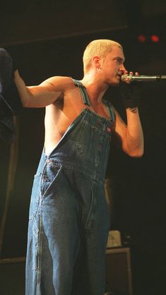 a man in overalls singing into a microphone with his hand on his hip and holding a towel