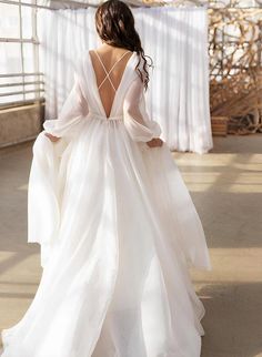 the back of a woman in a white wedding dress with long sleeves and flowing skirt