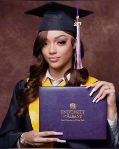 a woman wearing a graduation cap and gown holding a purple folder with the university of albany logo on it