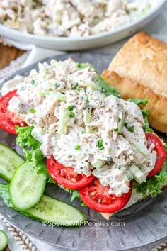 a chicken salad sandwich on a plate with cucumbers and bread in the background