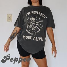 Elevate your Halloween spirit with our "I've Never Felt More Alive" shirt featuring a playful skeleton design, crafted from the soft and durable Comfort Colors fabric. This shirt is perfect for those who love to celebrate the season with a touch of spooky fun and style. Made from high-quality, pre-washed cotton, it ensures a soft, lived-in feel from the first wear and promises long-lasting comfort throughout the festivities. The striking skeleton graphic adds a unique and eye-catching element, making it an ideal choice for Halloween parties, trick-or-treating, or just embracing the Halloween season in style. Available in various sizes, this shirt makes a great gift for anyone who enjoys a blend of comfort and seasonal cheer. Whether you're looking for the perfect piece to wear on October 3 Oversized Skull Print T-shirt For Fall, Oversized Skull Print Crew Neck T-shirt, Relaxed Fit Tops For Halloween Streetwear, Oversized Casual Top With Skull Print, Relaxed Fit Skull Print Top For Halloween, Trendy Oversized Halloween Tops, Fall Oversized T-shirt With Skull Print, Trendy Oversized Tops For Halloween, Oversized Cotton Top With Skull Print