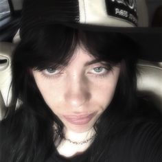 a woman with black hair wearing a hat and looking at the camera while sitting in a car