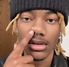 a young man with dreadlocks on his nose and finger under his nose ring