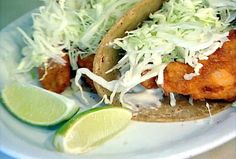 a white plate topped with fish covered in coleslaw and garnished with lime wedges