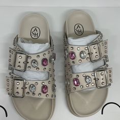 Ash Urge Buckle Sandals In White Leather & Gemstones The Ash Urge Sandals In An Off-White Leather Are Are A Two Strap Style Embellished With Gemstones And Studs Across The Upper. Off-White Leather Two Strap Style Silver Buckle Fastening Gemstone Embellishment Pool Slider New With Original Box, Dust Bag Designer Crystal Embellished Sandals For Summer, Leather Sandals With Rhinestones And Flat Heel, Leather Flat Heel Sandals With Rhinestones, Designer Leather Sandals With Rhinestones, Designer Rhinestone Sandals For Summer, Leather Sandals With Rhinestones For Beach, Designer Round Toe Sandals With Rhinestones, Designer Sandals With Rhinestones And Round Toe, Embellished Flat Beige Sandals