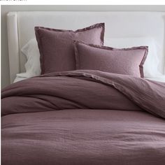 an unmade bed with purple linens and pillows