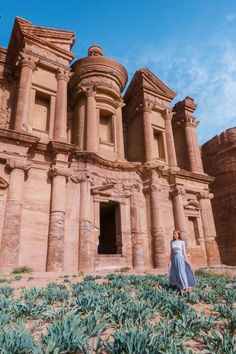 a woman standing in front of an ancient building with green plants growing on the ground