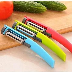 four different colored knives sitting on top of a cutting board next to cucumbers