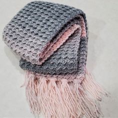 two knitted scarves on top of each other with pink and grey fringes