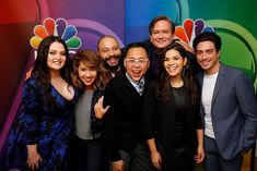 a group of people standing next to each other in front of a colorful wall with the nbc logo on it