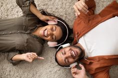 two people laying on the floor with headphones around their necks and pointing at something