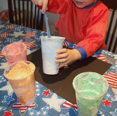 a young boy sitting at a table with two cups of ice cream in front of him