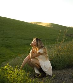 a woman sitting in the grass with her hands on her knees looking up at something