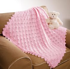 a white teddy bear sitting on top of a couch under a pink crocheted blanket