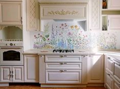 a kitchen with white cabinets and flowers painted on the wall behind the stove top oven