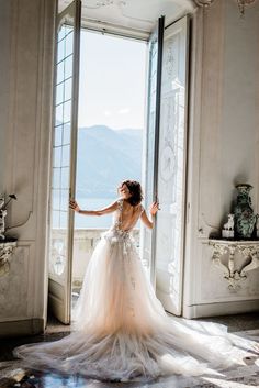 a woman in a wedding dress is standing by an open door with her arms outstretched