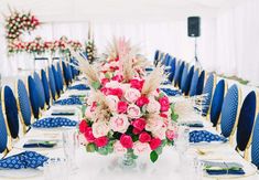 a long table with blue chairs and pink flowers in a vase on the centerpiece