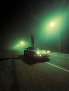 a man standing on top of a car in the middle of a road at night