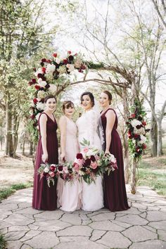 three bridesmaids stand in front of an arch decorated with flowers