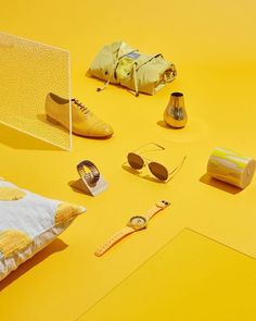 various items are arranged on a bright yellow surface, including sunglasses and other decorative objects