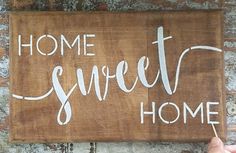 a wooden sign that says home sweet home on the side of a brick wall with someone holding a toothbrush