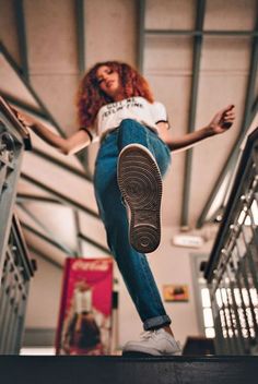 a woman is standing on the stairs with her feet in the air while wearing jeans and sneakers