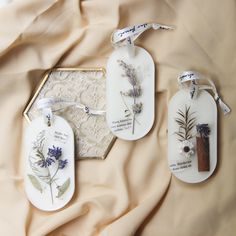 three tags with flowers on them are laying on a bed covered by a beige sheet