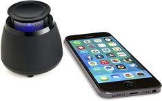 an iphone next to a black speaker with blue light on it's front and side