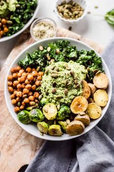 a white bowl filled with vegetables and nuts on top of a wooden cutting board next to other dishes