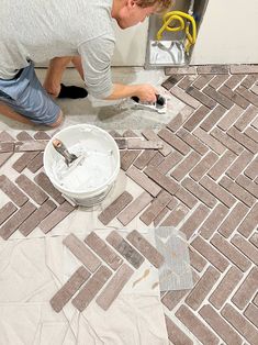 a man is working on some tiles in the bathroom floor with a paint bucket and brush