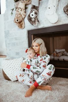 a woman and her baby are sitting in front of the fireplace wearing matching christmas pajamas