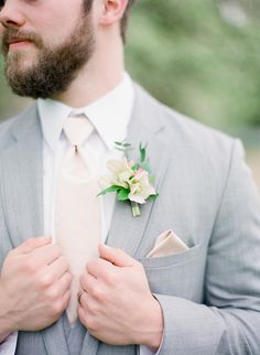 a man in a gray suit and white flower boutonniere with his hands on his chest