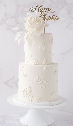 a three tiered white wedding cake sitting on top of a marble table next to a wall