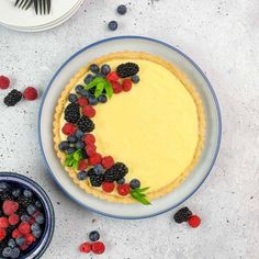 a cheesecake decorated with berries and leaves on a plate next to other desserts