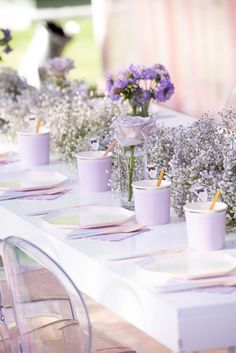 the table is set with purple flowers and cups