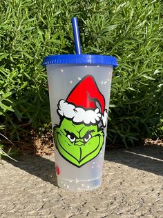 a plastic cup with a blue lid and a santa hat on it sitting in front of some bushes