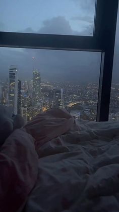 a person is laying in bed looking out the window at the city lights and skyscrapers