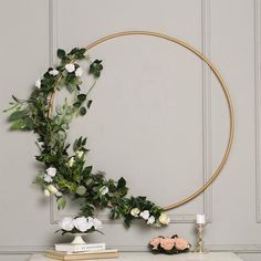 a white table topped with a gold circle frame and flowers next to a vase filled with roses