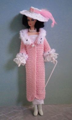 a doll wearing a pink crocheted dress and hat with white pom poms