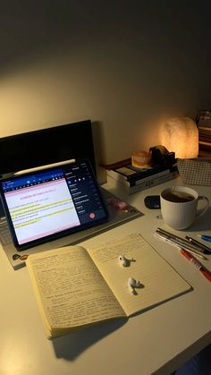 an open book sitting on top of a desk next to a laptop computer and cup of coffee