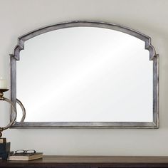 a mirror sitting on top of a wooden table next to a candle and a lamp