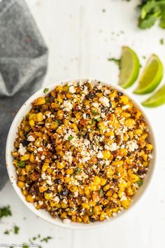 a white bowl filled with mexican street corn and topped with cilantro, lime wedges