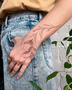 a person's hand with a tattoo on their left wrist and palm leaves on the right arm